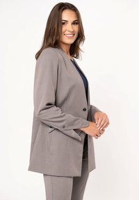 Gray tailored blazer with structured shoulders, single button closure, and subtle sheen. Pairing pants in a matching shade.