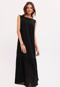 Czarna sukienka bez rękawów o prostym kroju, z falbaną na dole i lekkiego materiału. Prosty design bez wzorów.
