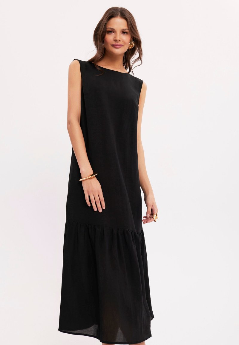 Czarna sukienka bez rękawów o prostym kroju, z falbaną na dole i lekkiego materiału. Prosty design bez wzorów.