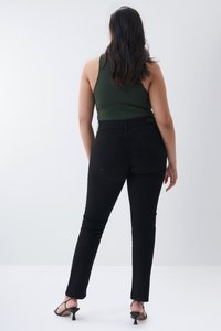 Jeans negros ajustados con una textura suave y diseño de cinco bolsillos, combinados con una blusa sin mangas de color verde oscuro, vistos desde la parte posterior.