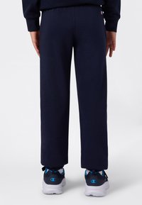 Marineblauwe sportbroek met een comfortabele pasvorm, elastische tailleband en geribbelde boorden; gecombineerd met sportieve schoenen met blauwe accenten.