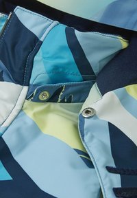 Wielokolorowa kurtka z niebieskim, zielonym i białym abstrakcyjnym wzorem. Posiada zapięcia na zatrzaski oraz gładką, lekką teksturę materiału.