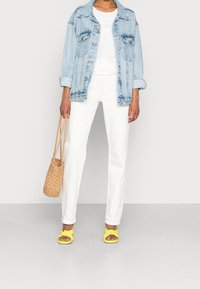 Giacca di jeans leggera blu, maglietta bianca in maglia, pantaloni bianchi a gamba dritta, sandali con fiocco gialli e borsa a tracolla intrecciata. Outfit semplice e moderno.