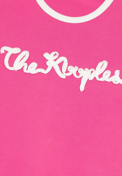 Roze katoenen t-shirt met verhoogde witte tekst die "The Krepples" zegt. Het heeft een ronde halslijn met witte afwerking. Over het algemeen een soepele textuur.