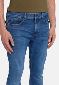 Jeans in denim blu a vestibilità slim, con design a cinque tasche e leggera scoloritura. Il tessuto appare morbido con una texture liscia e cuciture classiche.