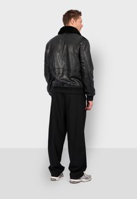 Černá kožená bomber bunda s beránkovým límcem, žebrovanými manžetami a pasem. Nosená s volnými černými kalhotami a teniskami, zobrazená zezadu.