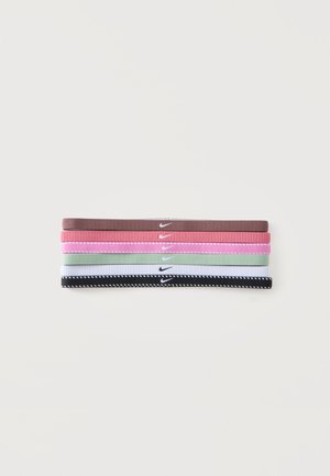Cinq bandeaux Nike pliés en marron, rose, rose clair, vert clair, blanc et noir avec des bords cousus sur fond blanc.