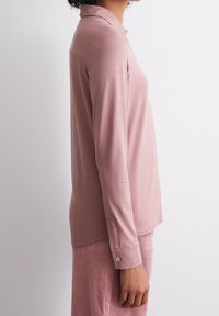 Långärmad, rosa polo skjorta i mjukt tyg, med krage och knappdetalj vid ärmen. Slät yta, figursydd design.