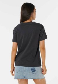 Camiseta de algodón negra con un corte holgado, mangas cortas y escote redondo, combinada con una falda de mezclilla ligera de color azul que presenta un detalle de diseño en la parte trasera.