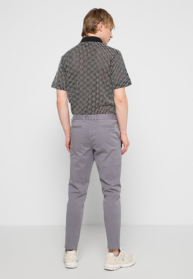 Koszula z krótkim rękawem w czarno-białe wzory, połączona z jasnoszarymi spodnie typu tapered. Obuwie to beżowe trampki.