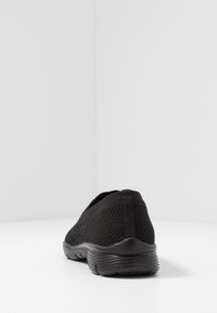 Czarne oddychające sneakersy z teksturowaną cholewką, bez zapięcia, elastyczną podeszwą i subtelną pętelką z tyłu ułatwiającą zakładanie.