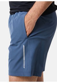 Blå shorts i lättviktsmaterial, med en sidficka och en reflektiv logodetalj för synlighet. Slät textur och skräddarsydd passform.