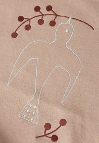 Brodert kunstverk med en fugl som er omrisset i lys blå på et mykt beige stoff, fremhevet av brune grener med sirkulære bær.