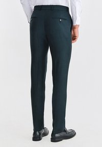 Ciemnozielone, dopasowane spodnie o gładkiej fakturze, z dwoma tylnymi kieszeniami zapinanymi na guziki oraz wąskim krojem.