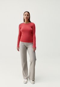 Długi rękaw, dopasowany, prążkowany czerwony top w połączeniu z jasnoszarymi, lekko teksturowanymi, rozszerzanymi spodniami. Obuwie to białe, płócienne sneakersy.