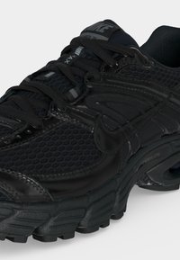 Μαύρο αθλητικό παπούτσι Nike με πλέγμα και δερμάτινο πάνω μέρος, παχιά μαλακή σόλα, ορατή αερόσολα και μαύρα κορδόνια.