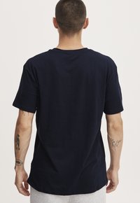 Tricou din bumbac bleumarin cu o croială relaxată, mâneci scurte și guler rotund. Design simplu, fără modele sau accesorii distincte.