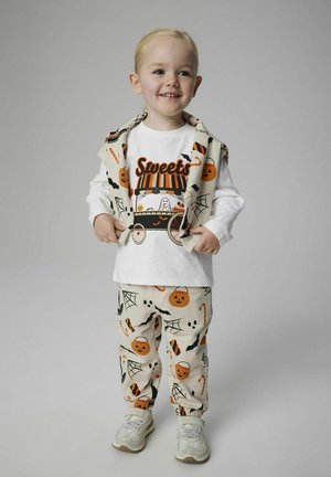 Uśmiechnięty maluch w przebraniu na Halloween, z nadrukiem dyni, pajęczyn, nietoperzy, lasek cukrowych i wózka ze słodyczami.