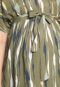 Green dress with multicolored abstract stripes in blue, white, and beige. Features a tied belt and short sleeves. Soft, textured fabric.