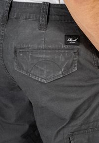 Graue Baumwollshorts mit einer strukturierten Oberfläche, die eine hintere Tasche mit einer geschwungenen Gestaltung und ein aufgenähtes Markenetikett am Bund aufweisen.