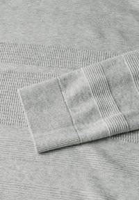 Pull en tricot gris clair avec des rayures texturées variées ; il présente des poignets côtelés et un tissu doux et lisse. Design minimaliste.