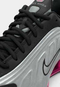 Czarno-szare sneakersy Nike Shox z grubymi czarnymi sznurowadłami i różowymi detalami na podeszwie, z logo Nike swoosh widocznym z boku.