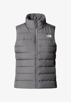 Pufová šedá vesta s vysokým límcem, zapínáním na zip a logem na levé hrudi; má vertikální prošívaný design a hladkou texturu.