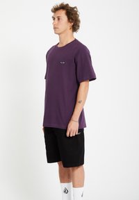 Paarse katoenen T-shirt met korte mouwen, ronde hals en klein merklogo op de borst, gecombineerd met zwarte shorts en witte sokken.