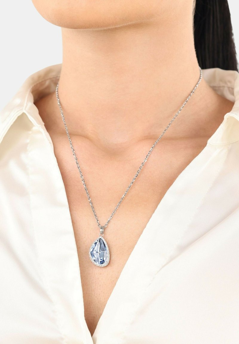 Collar de cadena de plata con un colgante de gema en forma de pera de color azul claro, rodeado por un borde decorativo; el engaste realza su superficie reflectante.