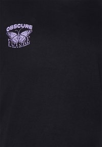 Musta t-paita, jossa on violetti grafiikka, joka esittää perhosta ja teksti "OBSCURE FUTURE FLY LIKE A BUTTERFLY" lihavoidulla fontilla.