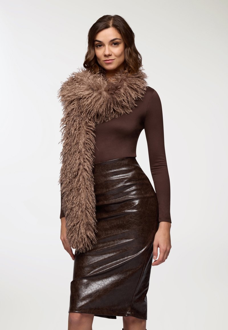 Scaldino di pelliccia sintetica marrone drappeggiato su una maglietta a maniche lunghe marrone aderente e una gonna a matita lucida marrone, che mette in mostra trame e colori intensi.