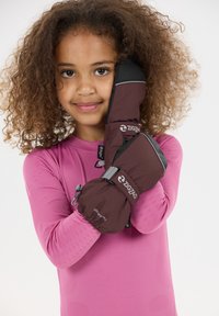 Des gants imperméables marron avec des accents noirs présentent un poignet élastique. Un enfant en haut à manches longues rose pose en tenant un gant contre sa joue.