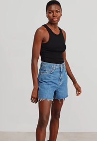 Top sin mangas negro combinado con pantalones cortos de mezclilla azul claro con bordes deshilachados y un ajuste relajado. Diseño sencillo sin patrones.