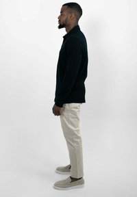 Schwarzes Longsleeve-Polohemd mit figurnaher Passform, kombiniert mit hellbeigen tapered Hosen und grauen Slippern.