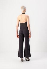 Crni halter top u kombinaciji s širokim, lepršavim sivim hlačama. Odjeća se odlikuje minimalističkim dizajnom i glatkom, teksturiranom tkaninom.