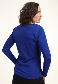 Camisa ajustada de manga larga hecha de una tela suave y de un brillante color azul. Presenta un cuello redondo y mangas ajustadas, sin patrones ni adornos visibles.