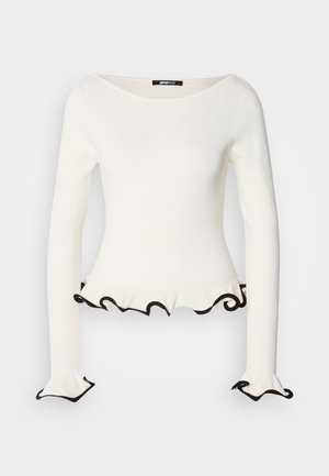Maglietta bianca a maniche lunghe con una silhouette aderente, caratterizzata da un bordo nero ondulato all'orlo e alle maniche. Realizzata in un materiale morbido ed elastico.