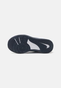 Sneaker talpa, amely texturált fekete gumi felülettel rendelkezik, körkörös és vízszintes mintázatokkal, valamint egy fehér akcentussal a ív területén.