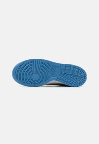 Plavi gumeni potplat tenisice s koncentričnim krugovima i horizontalnim utorima, s teksturiranom i glatkom površinom, uz detalje Nike logotipa.