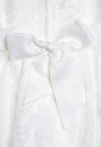 Vit klänning med ett strukturerat blommönster, åtdragen i midjan med en slät satinrosett knuten i en snygg knut.