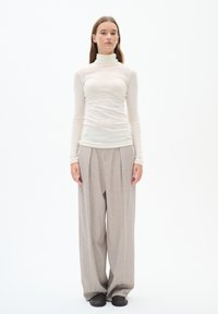 Turtleneck top in lightweight beige fabric, paired with wide-leg light gray trousers and dark slip-on shoes. Simple, minimalist design.