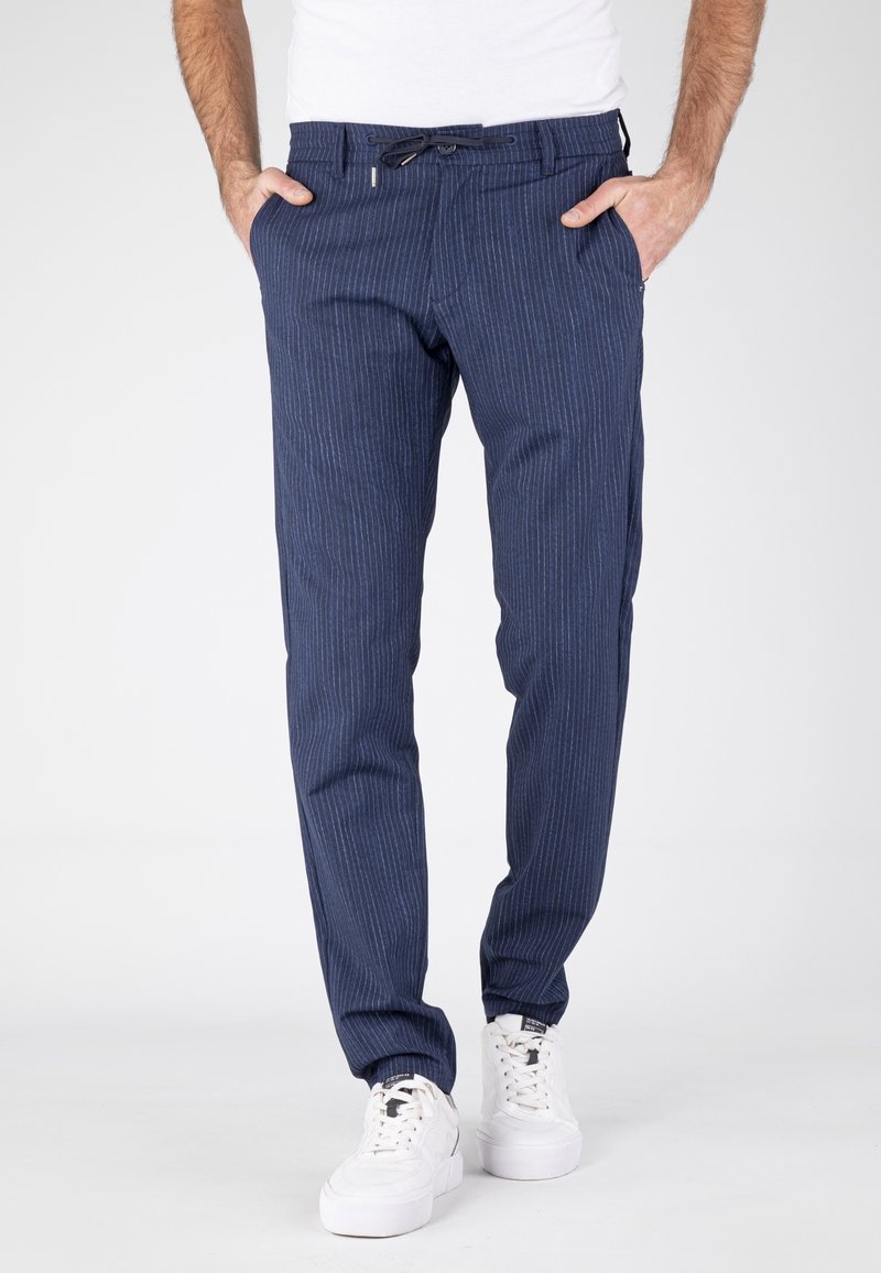 Chinos à rayures marine avec une coupe ajustée, taille à cordon, deux poches avant et poignets côtelés. Associés à des baskets blanches.