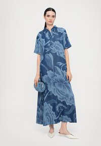 Rochie din denim cu mâneci scurte, model floral în nuanțe de albastru, design cu guler, lungime maxi, asortată cu o geantă texturată albastră și mule albe.