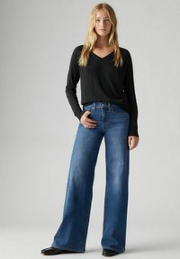 Zwarte lange mouwen v-hals trui gecombineerd met wijde blauwe spijkerbroek. De jeans hebben een klassiek vijf-pocket ontwerp en subtiele vervaging.