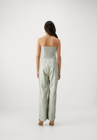 Jupe-pantalon sans bretelles de couleur vert clair avec un buste froncé, des pantalons à jambes larges et deux poches arrière, présentant une texture subtile et une coupe décontractée.