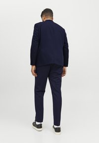 Marineblauer Anzug mit tailliertem Sakko und schmal geschnittenen Hosen. Glatte Stoffoberfläche; minimalistisches Design; detaillierte Nähte; kombiniert mit schwarzen Sneakers.