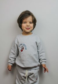 Completo felpa grigia e pantaloni della tuta con la scritta "ALPINE SKI CLUB" e una grafica di un impianto di risalita rossa. Materiale in cotone, vestibilità comoda e polsini a coste.