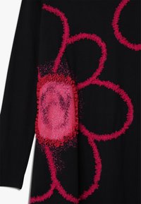 Czarna tkanina z intensywnymi różowymi, falbankowymi wzorami kwiatowymi, z wyraźnym, błyszczącym różowym akcentem w kształcie kwiatu na środku.