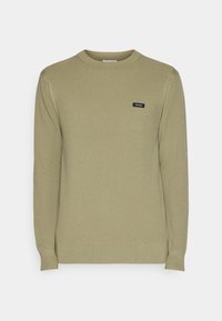 Pull tricoté vert olive clair à manches longues avec col rond et petite étiquette noire Calvin Klein sur le côté gauche de la poitrine.