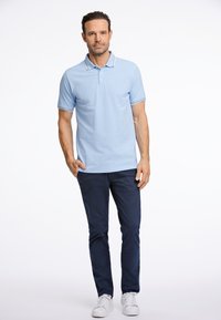 Camisa polo de color azul claro con mangas cortas y cuello, que presenta un ribete en contraste. Combinada con pantalones azul marino y zapatillas blancas. Fondo liso.